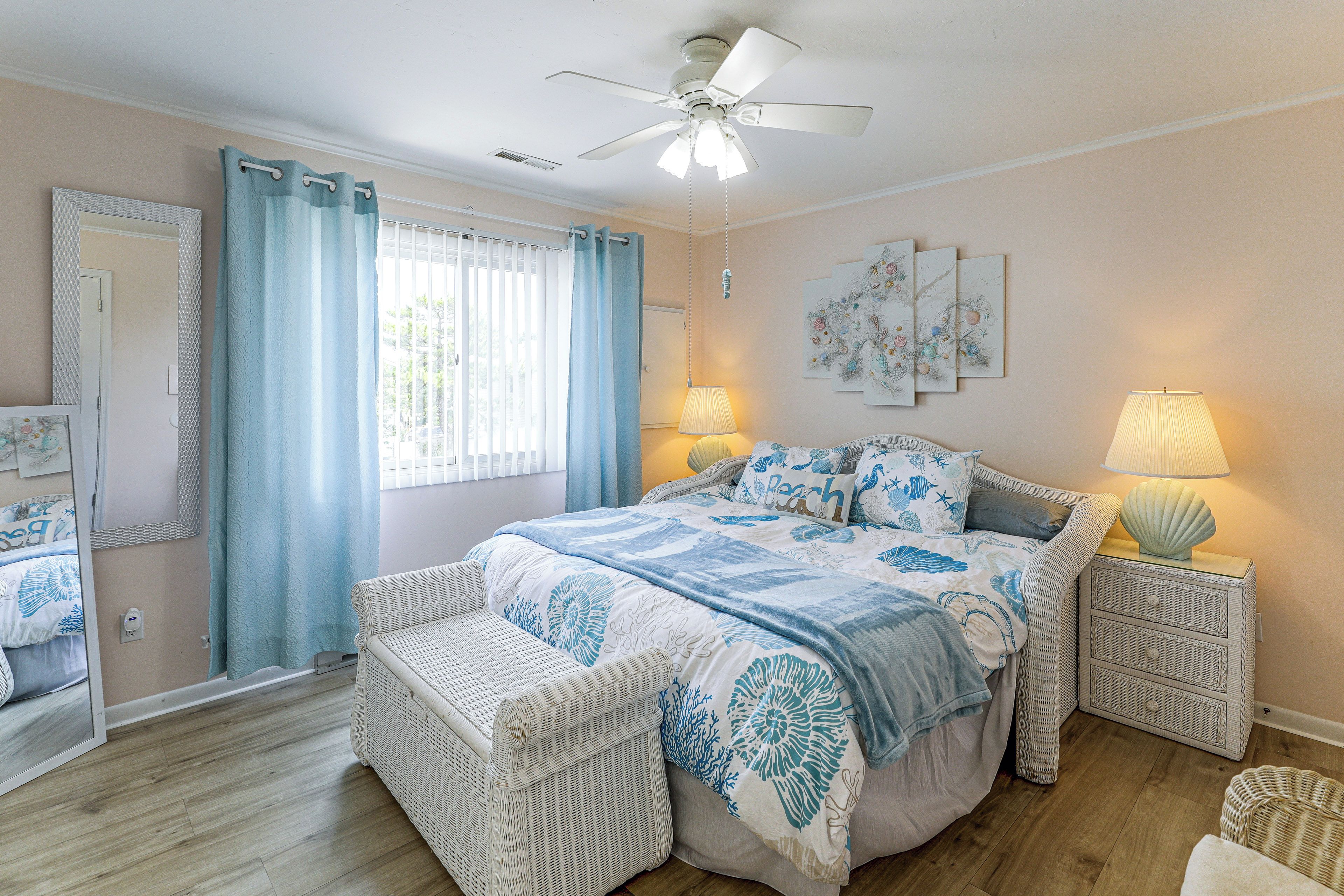 A bedroom with a bed, two bedside tables, a ceiling fan, a window with curtains, and wall art.
