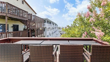 A balcony with wicker furniture overlooking a marina with boats, adjacent buildings, and blooming pink trees.