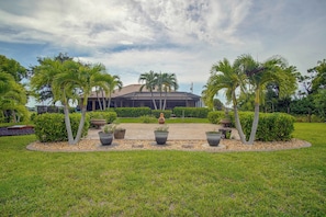 A landscaped garden with palm trees, a paved walkway, and a building with a tiled roof. - Private Yard w/ Fire Pit & Pool! Cape Coral Escape (Cape Coral)