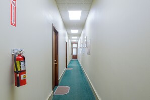 A hallway with a fire extinguisher mounted on the wall, a fire exit sign, and a door at the end.