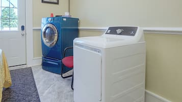 A laundry room with a blue and a white washing machine, a red chair, and a door with a window.