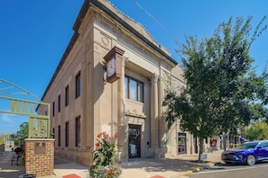 A classical building with a clock, a bench, and a tree in front.