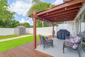 Eine Holzterrasse mit Gartenmöbeln, einem Grill und einem überdachten Patio.