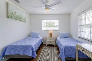 Ein Schlafzimmer mit zwei Einzelbetten, einem Deckenventilator, einem Fenster mit Jalousien und einem Nachttisch mit Lampe.
