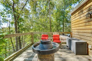 A wooden deck with a stone fire pit, red chairs, and a grill area.
