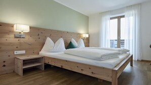 Una cama con estructura de madera, ropa de cama y almohadas blancas, una mesita de noche y una lámpara fijada a la pared.