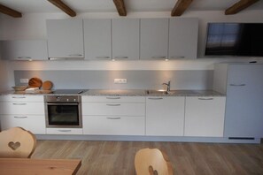 Cuina moderna amb armaris blancs, forn integrat, rentapelats i un televisor a la part superior.