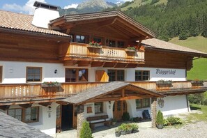 Ein traditionelles Holzchalet mit Balkon, einem Schild mit der Aufschrift 'Bruggerhof' und einem Bergpanorama im Hintergrund.