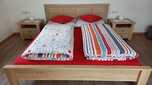 Una cama doble con cabecera de madera, dos mesitas de noche con lámparas y una colcha roja.