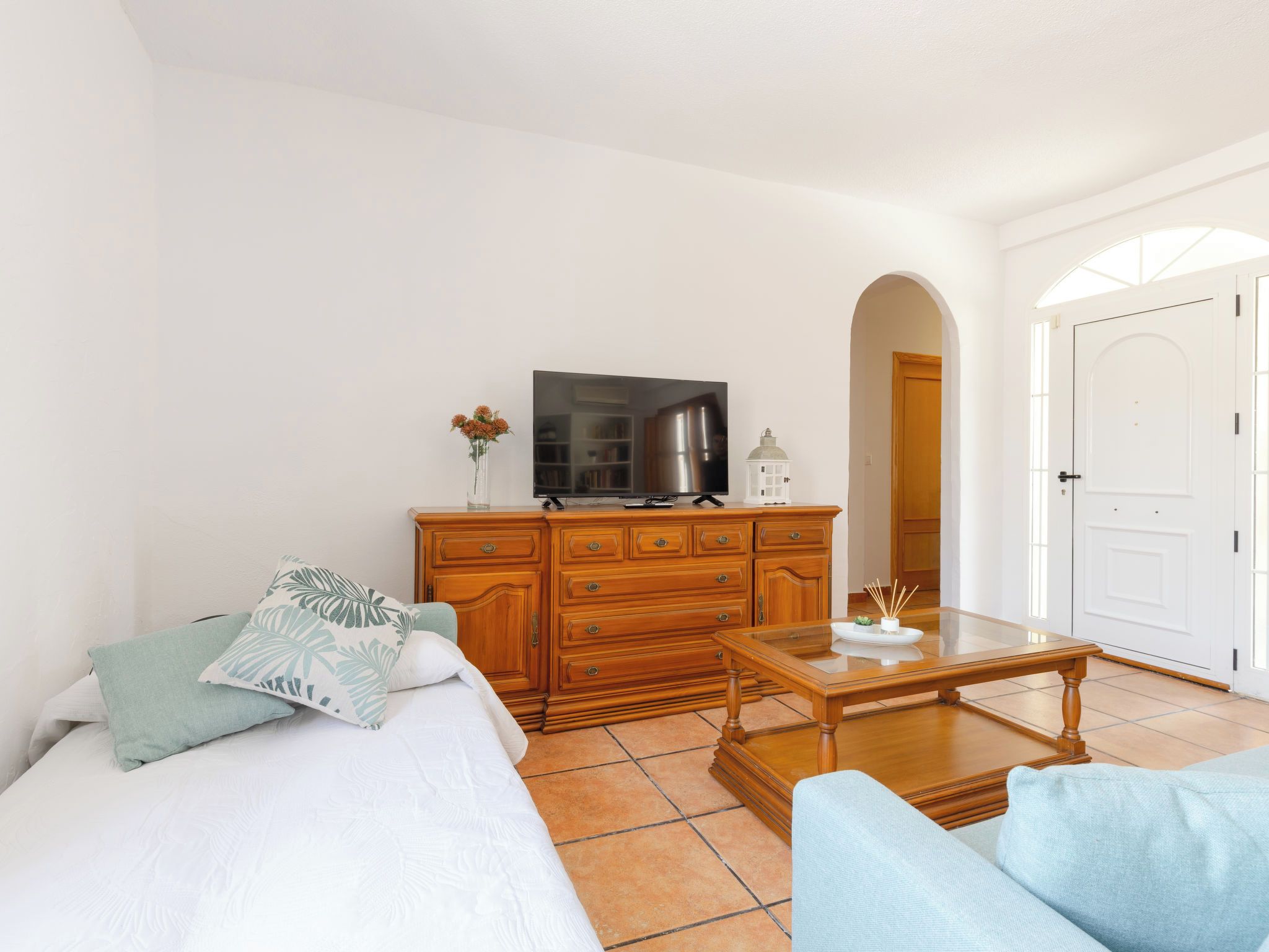Une pièce comprenant un lit, une commode en bois, un téléviseur et une porte donnant sur une autre pièce.