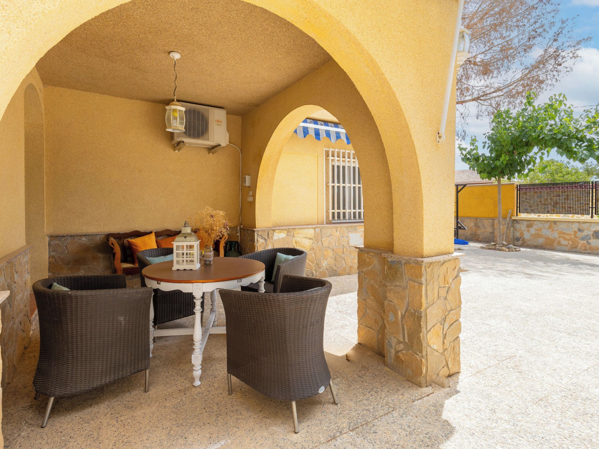 Une terrasse extérieure avec une table ronde, des chaises en osier et une lanterne décorative.