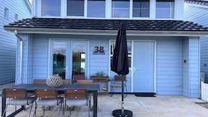 Ein blaues Haus mit der Nummer 38 an der Tür, eine Terrasse mit Tisch und Stühlen sowie ein schwarzer Sonnenschirm.