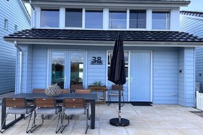 A blue house with a number '38' on the door, a patio with a table and chairs, and a black umbrella. - Holiday home with 1 bedroom (Wieringerwerf)