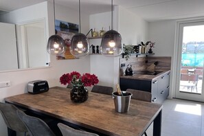 A modern kitchen with a wooden dining table, a toaster, a vase with red flowers, and a champagne bottle. - Holiday home with 1 bedroom (Wieringerwerf)