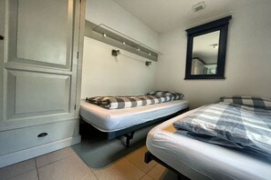 Een kleine kamer met twee bedden, een garderobe, een spiegel en een verlichte plank.