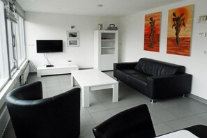 Een moderne woonkamer met een zwarte leren bank, een witte salontafel en een flatscreen televisie aan de muur.