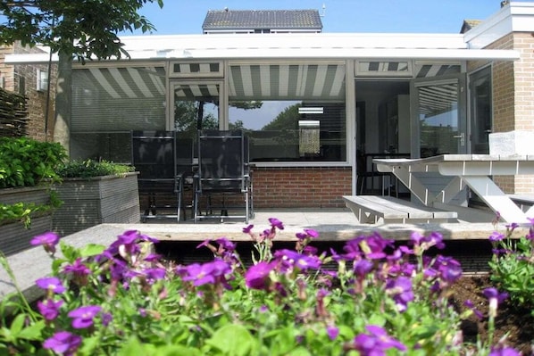 Een modern huis met een patio, een glazen deur die leidt naar een overdekt terras, en een bakstenen muur.