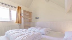 Ein Schlafzimmer mit zwei Betten, einem Fenster mit Vorhängen und einem weißen Kopfteil.