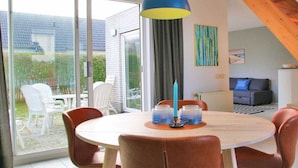 Ein Essbereich mit einem runden Tisch, Stühlen, einer blauen Pendelleuchte und Blick durch Glastüren auf eine Außenpatio.