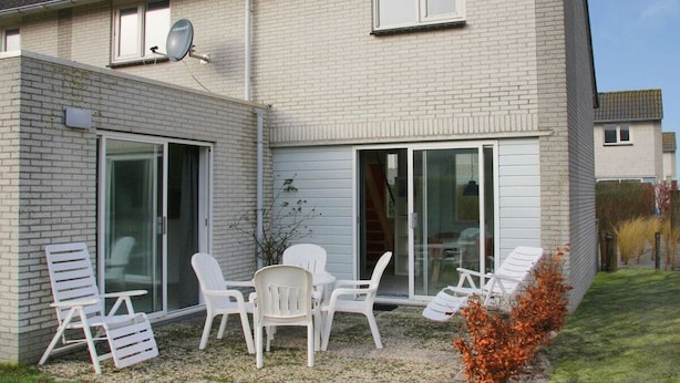 Ein zweistöckiges Haus mit einer Terrasse, ausgestattet mit weißen Kunststoffstühlen und einem Tisch.
