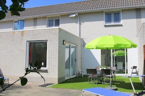 A residential building with a patio area, a green umbrella, and outdoor furniture. - De C"oogse Strandloper (Callantsoog)
