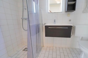 A bathroom with a glass shower enclosure, a white sink with a black cabinet, and a white toilet. - De C"oogse Strandloper (Callantsoog)