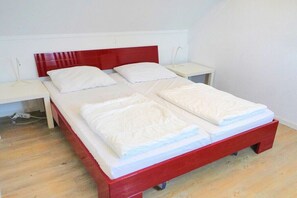 A single bed with a red headboard and white bedding in a room with a wooden floor. - De C"oogse Strandloper (Callantsoog)