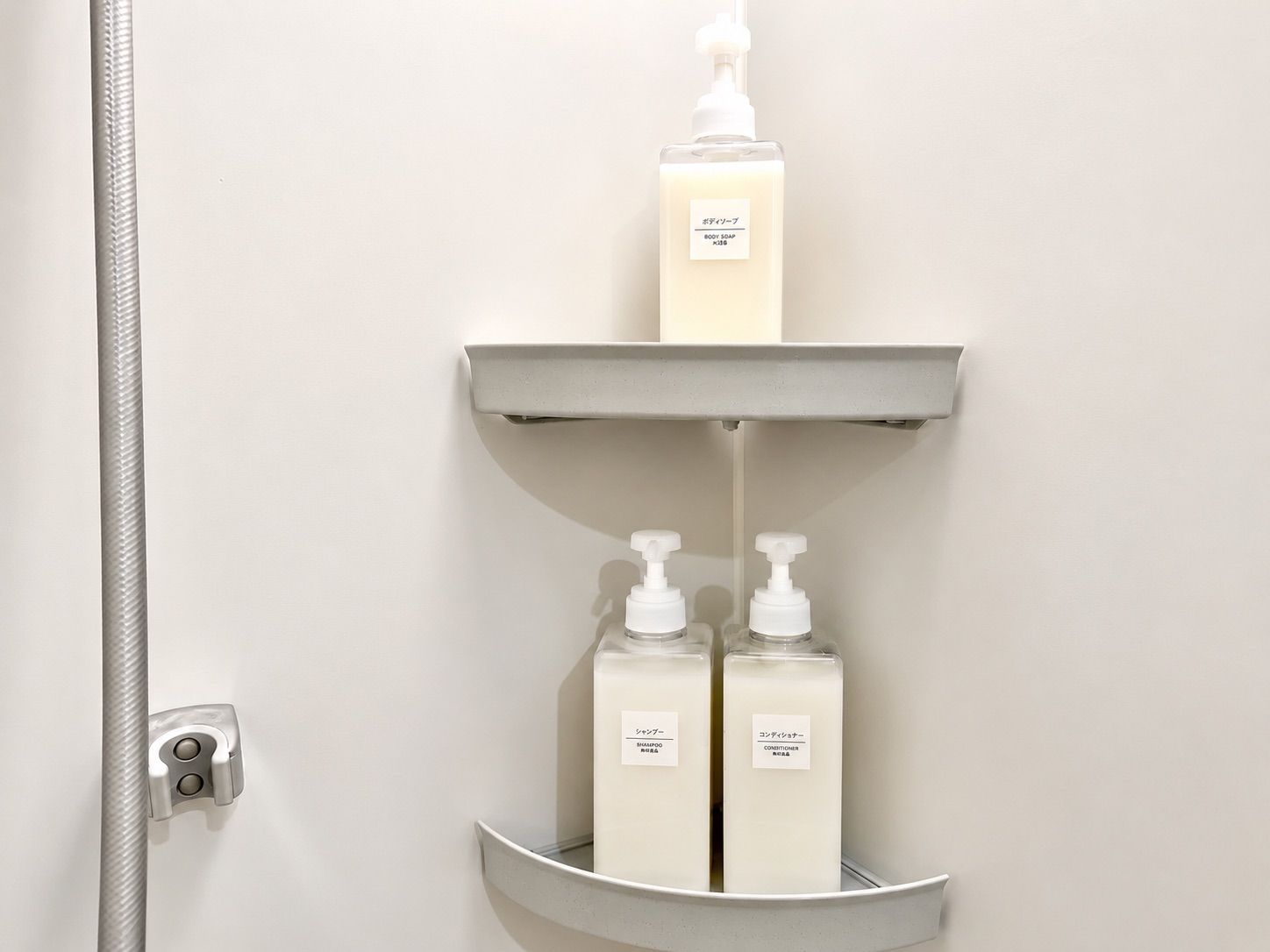 A bathroom with a shower, a soap dispenser, and two bottles of shampoo and conditioner.