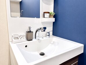 A modern bathroom with a white sink, chrome faucets, and a mirror above. - Vrbo Property (大阪市西区九条南3-19)