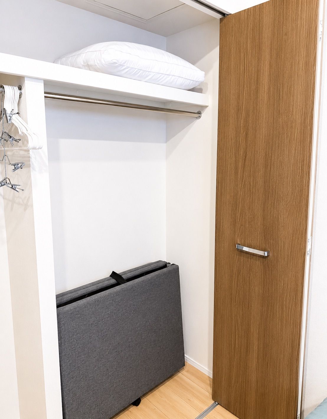 A walk-in closet with a wooden door, a white hanging rod, and a grey storage bench.