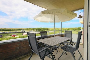 A balcony with a table and chairs, an umbrella, and a view of a parking lot and greenery. - Holiday apartment in Groote Keeten with Wi-Fi (Groote Keeten)