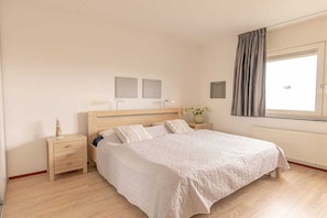A bedroom with a wooden bed, a nightstand, a window with curtains, and a wall-mounted light fixture. - Holiday apartment in Groote Keeten with Wi-Fi (Groote Keeten)
