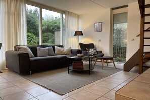 A living room with a sofa, a chair, a coffee table, and a lamp. There is a staircase to the right. - Holiday home with 1 bedroom (Sint Maartensbrug)
