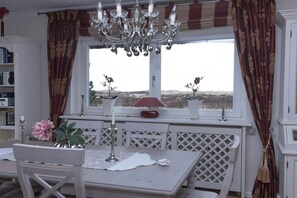 Ein Essbereich mit Tisch, Stühlen, einer Deckenleuchte und Blick durch ein Fenster.