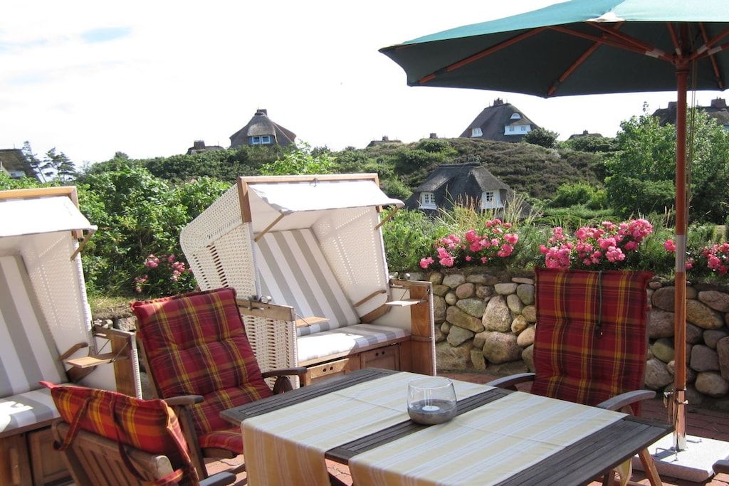 Ein Sitzbereich im Freien mit Stühlen und einem Tisch, umgeben von einer Steinmauer und blühenden Pflanzen.