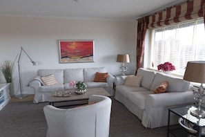 Ein Wohnzimmer mit zwei weißen Sofas, einem Couchtisch, einer Lampe und einem Gemälde an der Wand.