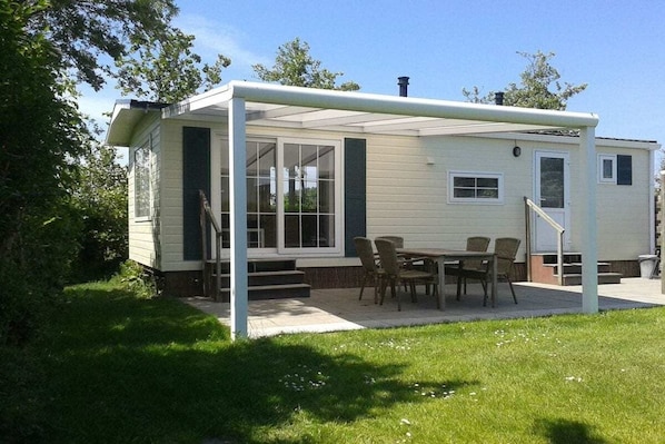 En etagers mobilhome med en overdækket terrasse, spisebord og stole.