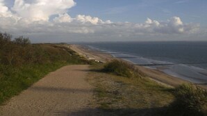 Un sentier côtier qui mène à une plage offrant une vue dégagée sur la mer et l’horizon lointain.