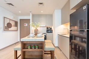 A modern kitchen with a built-in refrigerator, a microwave, and a coffee machine. There is a dining area with a table set for four, a vase with flowers, and a small shelf with plants. - Chic 1BR with Outdoor Terrace, Minutes from Downtown Dubai (Dubai)
