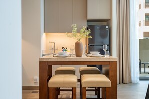 A modern kitchen with a built-in refrigerator, a dining table with two cushioned chairs, and a vase with flowers on the countertop. - Chic 1BR with Outdoor Terrace, Minutes from Downtown Dubai (Dubai)