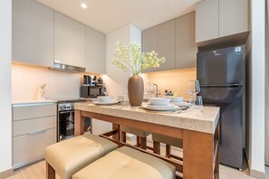 A modern kitchen with a built-in oven, a refrigerator, and a dining area with a vase of flowers. - Chic 1BR with Outdoor Terrace, Minutes from Downtown Dubai (Dubai)