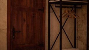 Una habitación con puerta de madera, un perchero metálico con ropa y una cama.