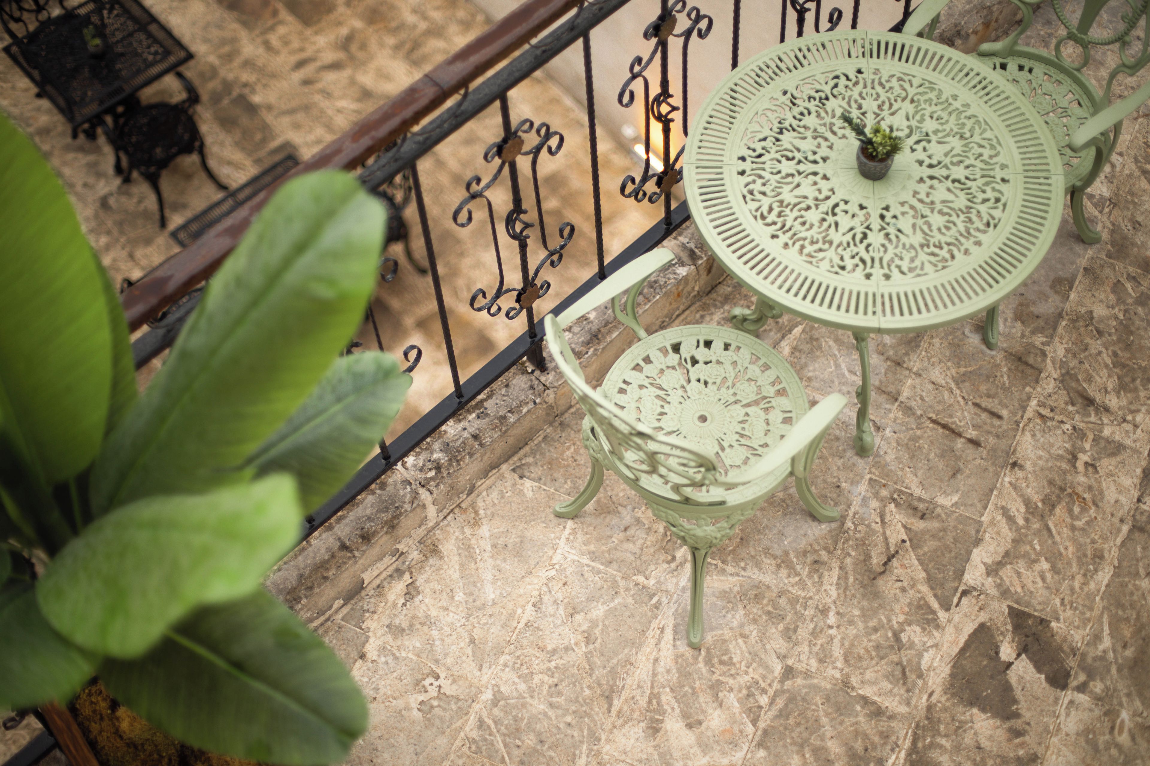 A balcony with wrought iron railings, a green metal table with intricate designs, and a matching chair.