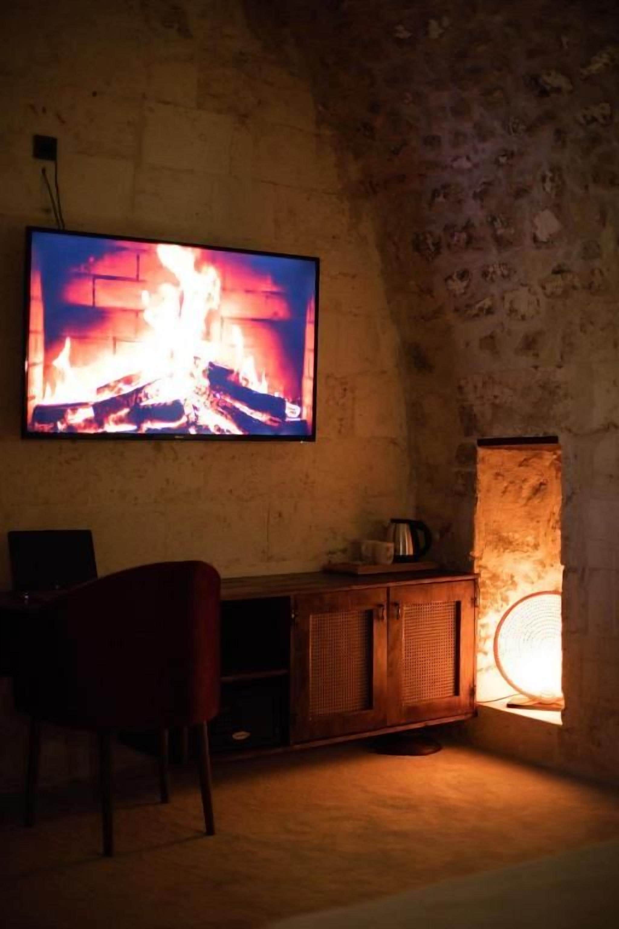 Una habitación con un televisor montado en una pared de piedra, un armario de madera y una silla.