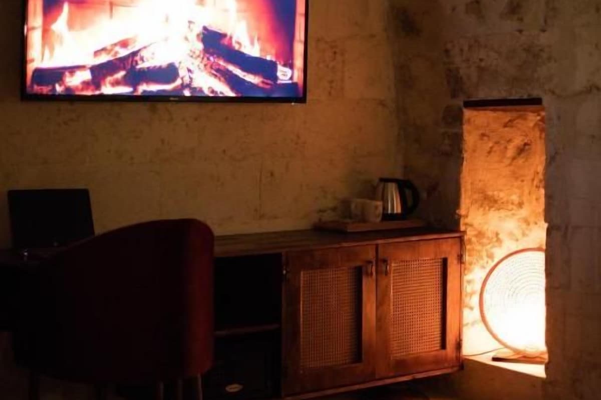 A room with a television mounted on a stone wall, a wooden cabinet, and a chair.