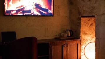 Una habitación con un televisor montado en una pared de piedra, un armario de madera y una silla.