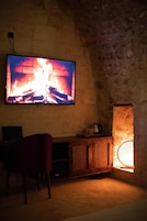 Una habitación con un televisor montado en una pared de piedra, un armario de madera y una silla.