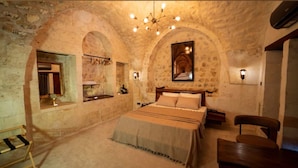 A bedroom with a large bed, a wooden headboard, a hanging light fixture, and stone walls. - HOTEL ESTARA (Şanlıurfa)
