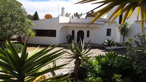 A white building with a tiled roof, surrounded by a garden with various plants and a paved courtyard. - Holiday home with 3 bedrooms (Carvoeiro LGA)