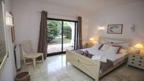 A bedroom with a bed, a chair, a nightstand, a lamp, and a view of the outdoors. - Holiday home with 3 bedrooms (Carvoeiro LGA)